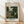May include: Framed art print displayed against white wall on wooden floor. Print features lush tropical jungle scene with dense green foliage, palm fronds, and exotic plants in Henri Rousseau's distinctive naive style. Light wooden frame surrounds cream-colored poster with blue text reading "The Equatorial Jungle" and "Henri Rousseau 1909" along with "The National Gallery of Art." Natural lighting creates soft shadows on textured white wall.