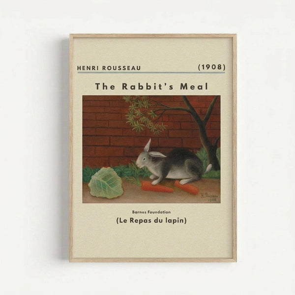 A framed art print featuring Henri Rousseau's 1908 painting of a gray and white rabbit sitting beside fresh vegetables including a large green cabbage leaf and orange carrots. The scene shows a brick wall background with a small tree, painted in Rousseau's characteristic naive style with muted earth tones. The print has cream matting with black text identifying the artist, date, and French title, all contained within a natural wood frame against a white wall.