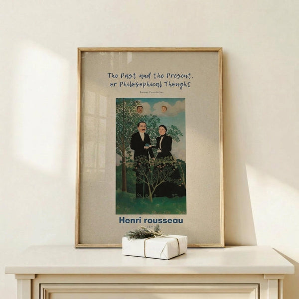 May include: Framed reproduction poster of naive art painting showing two men in dark suits standing in lush green landscape with trees and clouds, faces appearing in sky above. White matted print in natural wood frame displayed on light wooden surface beside small white wrapped gift with twine and greenery sprig against cream wall.