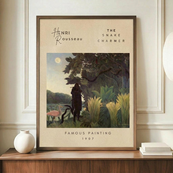 May include: Framed art print displayed on wooden credenza in neutral room setting. Print features jungle scene with silhouetted figure playing flute near water, surrounded by lush tropical foliage, pink flamingo, and full moon in dusky sky. Cream matting with brown frame. White ceramic vase and stacked books nearby.