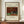 May include: Framed art print displaying Henri Rousseau's 1908 painting of a gray rabbit sitting beside orange carrots and green cabbage against a red brick wall with tree branches. The cream-colored poster shows museum-style text above and below the artwork. Displayed on wooden sideboard with white ceramic vase and stacked books in bright room with white wainscoting.