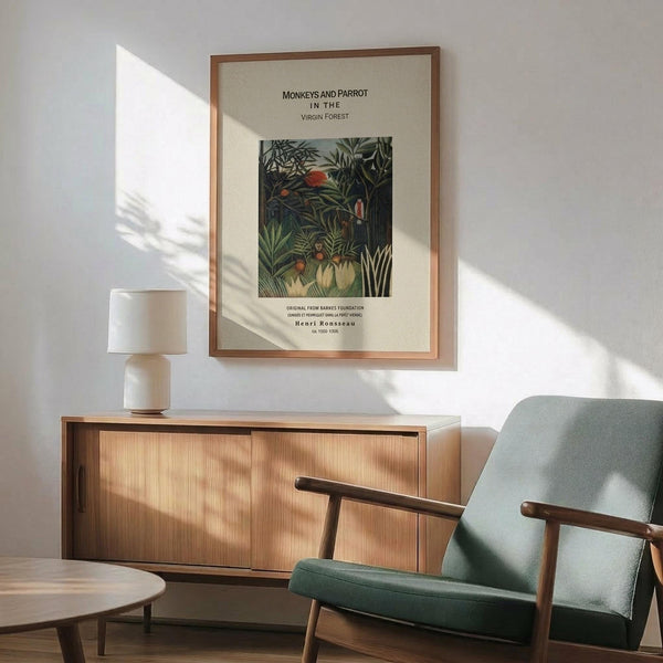 May include: Framed Henri Rousseau jungle print featuring monkeys and parrot among lush green foliage, displayed above wooden sideboard with table lamp in modern living room. Mid-century furniture with sage green upholstered chair, warm sunlight casting shadows across white wall. Print shows dense tropical vegetation in dark greens with colorful birds.