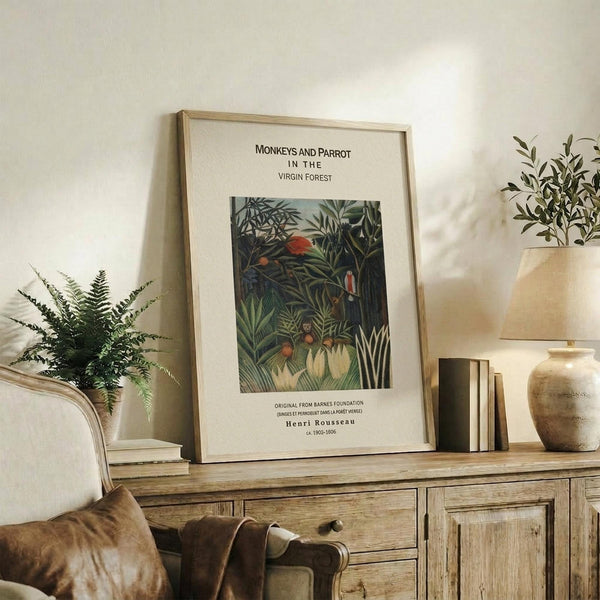 May include: Framed botanical art print featuring jungle scene with monkeys and colorful parrot among lush green foliage, displayed on rustic wooden sideboard alongside fern plant, ceramic vase, and books in neutral-toned living room setting with cream upholstered furniture.