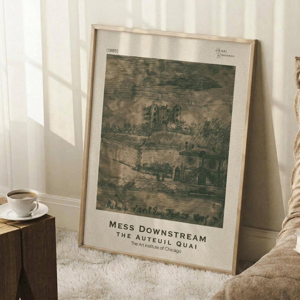 May include: Framed vintage-style art print leaning against white paneled wall on white shag rug. Print shows green-toned landscape with buildings and hills, dated 1885, with museum exhibition text below. Light wood frame, coffee cup on wooden block nearby, neutral decor setting with soft natural lighting.