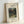 May include: Framed art print leaning against white wall showing Henri Rousseau's jungle painting with monkeys and a red parrot among dense green tropical foliage. Light wood frame with white matting displays the vintage botanical artwork with museum-style text labels above and below the image.