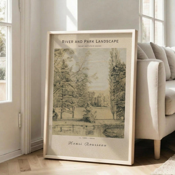 May include: Framed vintage landscape artwork showing trees, water, and parklike scenery in muted earth tones, leaning against white wall next to beige upholstered chair. Natural lighting from nearby windows creates soft shadows on light wooden floors. The print appears museum-style with cream matting and light wood frame.