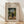 May include: Framed museum-style art print featuring Henri Rousseau's painting of a man in dark suit and hat standing beside a small child in white dress on a tree-lined path. The vintage-inspired poster has beige background with black text reading "Stroller and Child" and museum details. Natural wood frame leans against white wall on light wooden floor with soft window shadows.