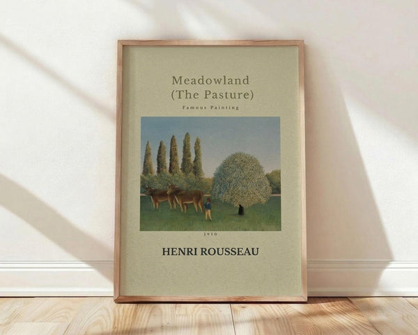 May include: Framed art print leaning against white wall on light wooden floor. Features Henri Rousseau's pastoral painting with brown cows grazing in green meadow, tall cypress trees, and large rounded tree. Cream-colored background with black text and 1910 date. Natural wood frame with visible grain. Soft shadows cast on textured white wall.