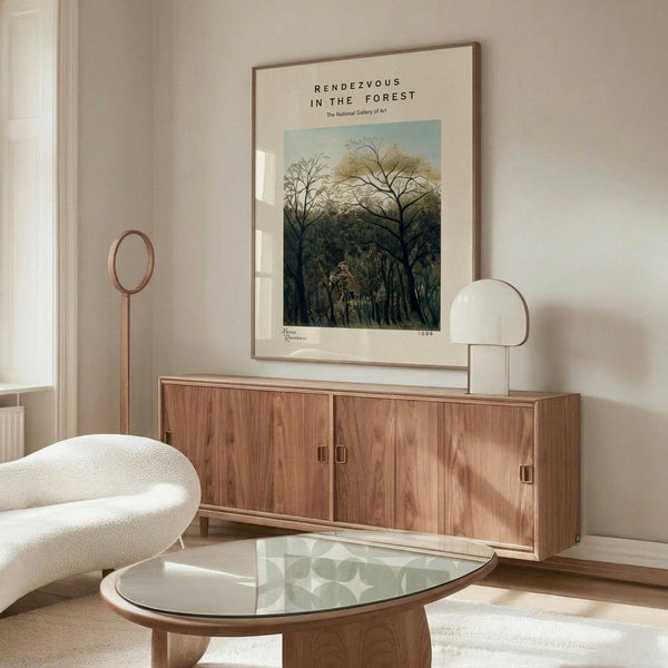 May include: Framed poster print featuring a lush forest scene with tall trees and dense foliage in greens and earth tones, displayed above a wooden sideboard with sliding doors in a modern living room setting. White sculptural chair and glass-top coffee table visible in foreground, with warm natural lighting creating shadows on cream walls.