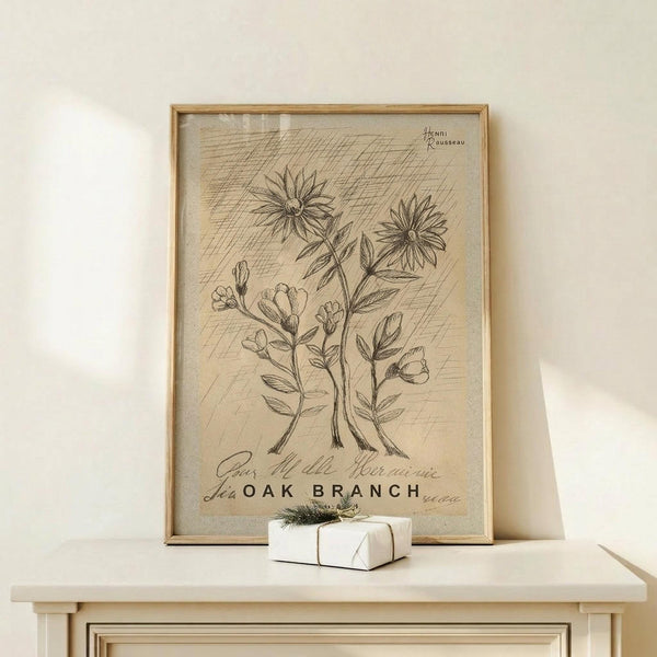 May include: Vintage botanical illustration print in wooden frame showing hand-drawn flowers and stems with French text "Oak Branch" below. The artwork has sepia tones on aged paper background with cross-hatching details. Frame sits on light wooden surface next to small white wrapped gift with twine and greenery accent against cream wall.