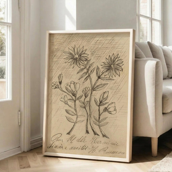 May include: Large framed botanical illustration print in light wood frame, leaning against white wall next to beige upholstered chair. The vintage-style artwork features detailed pencil drawings of flowering plants and leaves on aged paper background with handwritten script text below. Natural lighting from nearby windows creates soft shadows in minimalist living room setting.