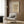 May include: Botanical wall art print featuring vintage-style illustration of oak branch with flowers and leaves on cream background, displayed in light wooden frame on warm brown wood paneled wall above beige upholstered armchair with geometric patterned pillow, brass floor lamp and dark side table visible in modern neutral-toned interior setting
