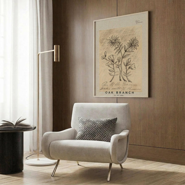 May include: Botanical wall art print featuring vintage-style illustration of oak branch with flowers and leaves on cream background, displayed in light wooden frame on warm brown wood paneled wall above beige upholstered armchair with geometric patterned pillow, brass floor lamp and dark side table visible in modern neutral-toned interior setting