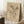 May include: Vintage-style botanical illustration print in thin light wood frame, leaning against white wall corner. Features hand-drawn flowers including daisies and smaller blooms with stems and leaves, rendered in brown ink on cream background with crosshatch shading. Cursive text appears at bottom. Positioned on white textured rug beside wooden block with coffee cup and neutral throw blanket. Soft natural lighting creates gentle shadows.