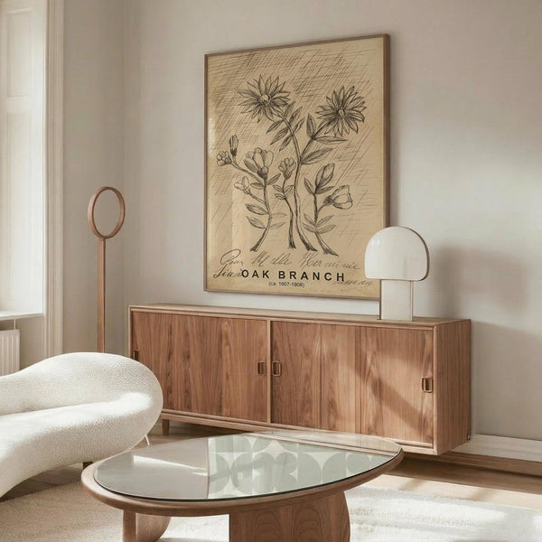 May include: Vintage botanical illustration poster displayed above walnut credenza in modern living room. Cream-colored artwork shows detailed pen and ink drawings of flowering plants with cross-hatched background texture, mounted in thin wooden frame. Room features curved white chair, glass oval coffee table, and minimalist table lamp, creating warm neutral interior styling.