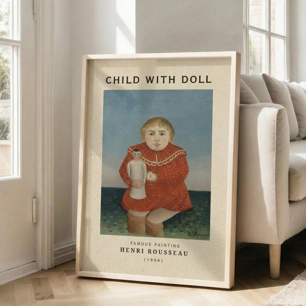 May include: Framed art print leaning against beige sofa in bright living room with white walls and windows. Print features naive-style painting of blonde child in red polka dot dress holding small doll, seated against blue and green background. Text reads "Child with Doll" and "Famous Painting Henri Rousseau (1906)" on cream colored border around artwork.