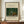 May include: Framed art print of tropical jungle scene with banana trees and two small figures beneath thatched shelter, displayed on wooden credenza next to white ceramic vase and stacked books against cream colored wall with white trim molding.
