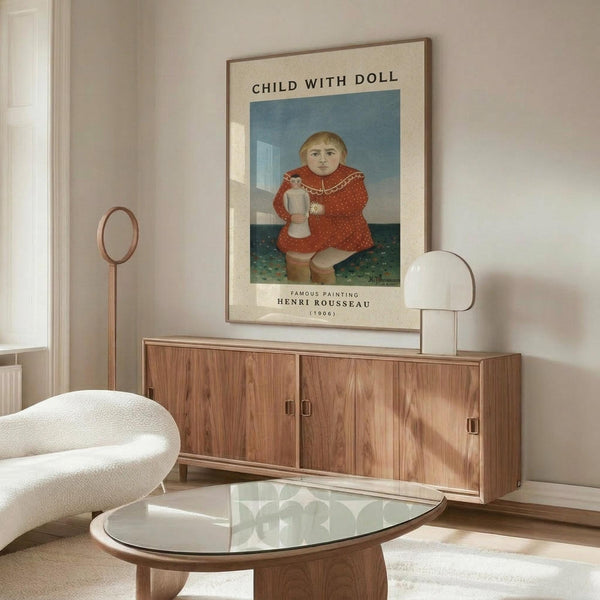 May include: Henri Rousseau reproduction poster showing child in red dress holding white doll, displayed in modern living room with walnut credenza, white sculptural chair, glass coffee table, and minimalist decor. The vintage-style art print features muted colors and naive painting style typical of early 1900s folk art.