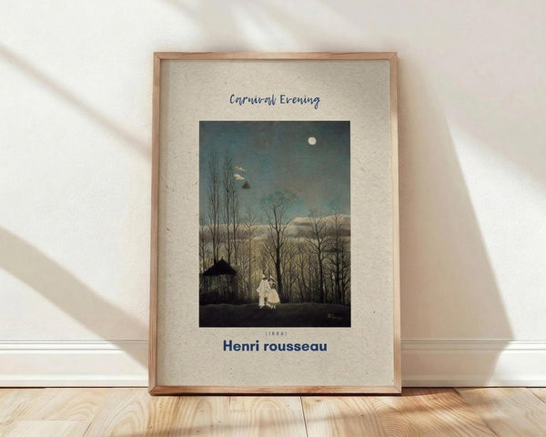 May include: Framed art print featuring Henri Rousseau's 1886 painting "Carnival Evening" showing two white-costumed figures standing beneath bare winter trees under a full moon in a dusky blue-green sky. The vintage-style poster has cream colored matting with the artist's name in blue text below the image. Wooden frame sits on light wood flooring against white wall with natural window light casting shadows across the scene.