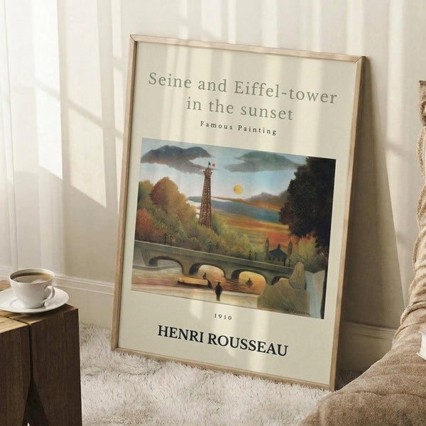 May include: Framed art print leaning against white wall corner featuring Eiffel Tower and Seine river landscape in autumn colors with bridge and trees. Light wood frame on white matting, positioned on textured white rug next to wooden side table with coffee cup. Natural lighting creates soft shadows across the scene.