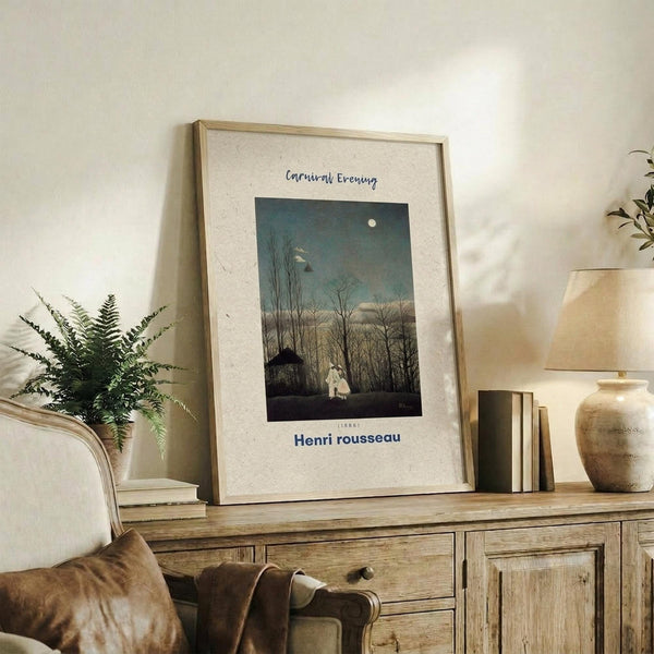 May include: Framed art print featuring a moonlit evening scene with bare trees, small house, and white figure against a dusky blue-green sky. The poster has cream matting with the artist's name below the image. Displayed on a rustic wooden sideboard alongside a fern plant, stacked books, ceramic lamp, and clay vase in a neutral-toned living room setting.