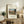 May include: Framed art print featuring Henri Rousseau's painting of the Eiffel Tower and Seine River at sunset, displayed on a rustic wooden sideboard alongside books, a ceramic vase, fern plant, and table lamp in a cozy living room setting with neutral tones and warm lighting.
