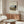 May include: Framed art print featuring Henri Rousseau's 1910 painting of the Seine River and Eiffel Tower at sunset, displayed above a wooden sideboard with sliding doors in a modern living room. White upholstered chair, glass-top oval coffee table, and minimalist decor complete the neutral-toned interior scene.