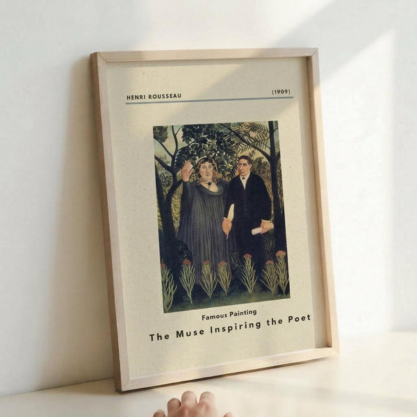 May include: Framed art print leaning against white wall showing Henri Rousseau's 1909 painting "The Muse Inspiring the Poet" featuring two figures in dark clothing standing among lush jungle foliage. Print has cream matting with black text identifying the artist, date, and title. Light wooden frame casts soft shadow on wall. Partial view of hand in corner for scale reference.