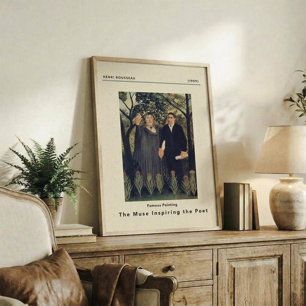 May include: Framed art print of Henri Rousseau's 1909 painting showing two figures in dark clothing surrounded by lush jungle foliage, displayed on a rustic wooden sideboard alongside a fern plant, stacked books, and ceramic pottery in a warm, neutral-toned living room setting.