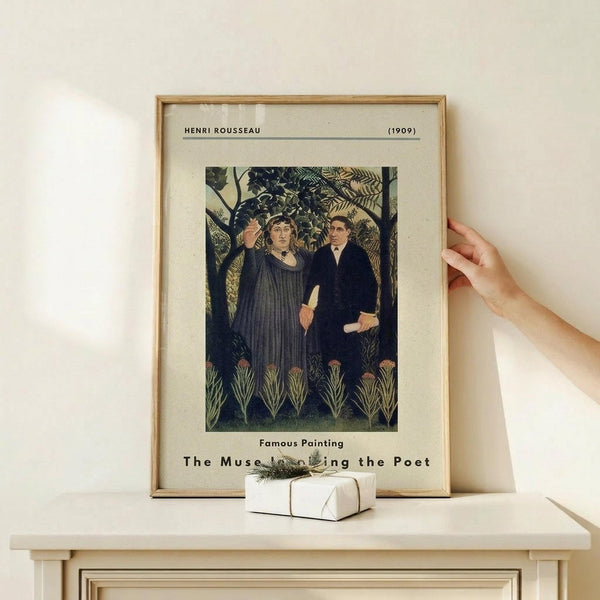 May include: Framed art print displaying Henri Rousseau's 1909 painting featuring three figures in dark clothing standing among lush green tropical foliage. The vintage-style poster has cream matting and thin wooden frame, positioned on a light wood shelf against white wall. A hand reaches toward the frame from the right side, with a small white wrapped gift box sitting on the shelf below the artwork.