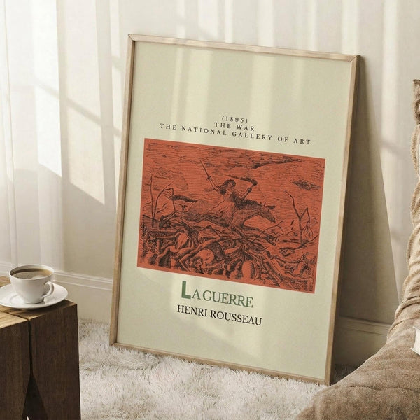 May include: Framed vintage art print leaning against white wall on fluffy white rug. Print shows red-orange illustration of figure in dynamic scene with "LAGUERRE HENRI ROUSSEAU" text below. Light wood frame, coffee cup on wooden block nearby, beige blanket visible at edge. Natural lighting creates soft shadows.