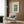 May include: Vintage-style poster of Mount Fuji with cherry blossom tree and lake in soft blues and pastels, displayed in light wooden frame on wood-paneled wall above beige upholstered armchair with geometric patterned pillow, alongside brass floor lamp and dark side table with open book