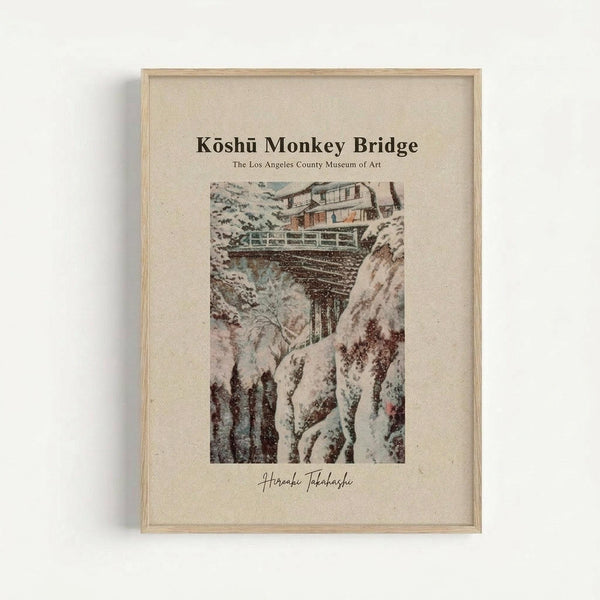 May include: Framed vintage Japanese woodblock print showing a snow-covered wooden bridge spanning a rocky winter gorge. The artwork features muted colors with white snow, brown wooden structures, and rocky cliffs. Text reads "Koshu Monkey Bridge" and "The Los Angeles County Museum of Art" with an artist signature below. Light wood frame against white wall background.