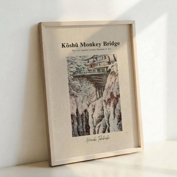 May include: Framed vintage Japanese woodblock print poster showing a snow-covered wooden bridge spanning a rocky winter gorge. The artwork features muted earth tones with white snow, displayed in a light wood frame against a white wall. The print includes museum attribution text at the top and artist signature at the bottom on cream-colored paper.