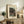 May include: Framed vintage Japanese woodblock print showing figures under moonlit trees by water, displayed on rustic wooden sideboard beside fern plant, lamp, ceramic vase and books in neutral-toned living room setting