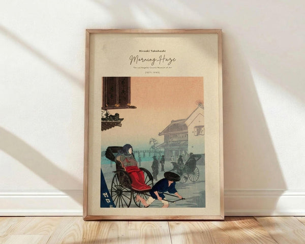 May include: Framed vintage Japanese woodblock print showing a woman in red kimono sitting in a black rickshaw, with a man pulling it through a misty street scene. The artwork features soft peach and blue tones depicting traditional buildings and other carriages in the background. Displayed in a light wooden frame against white walls on blonde hardwood floors with natural window light casting shadows.
