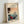 May include: Light wooden frame displaying a vintage Japanese woodblock print showing people with rickshaws on a misty street scene in soft peach, teal and coral tones. Frame leans against white wall on light surface, showing museum-style text at top with artist name and dates.