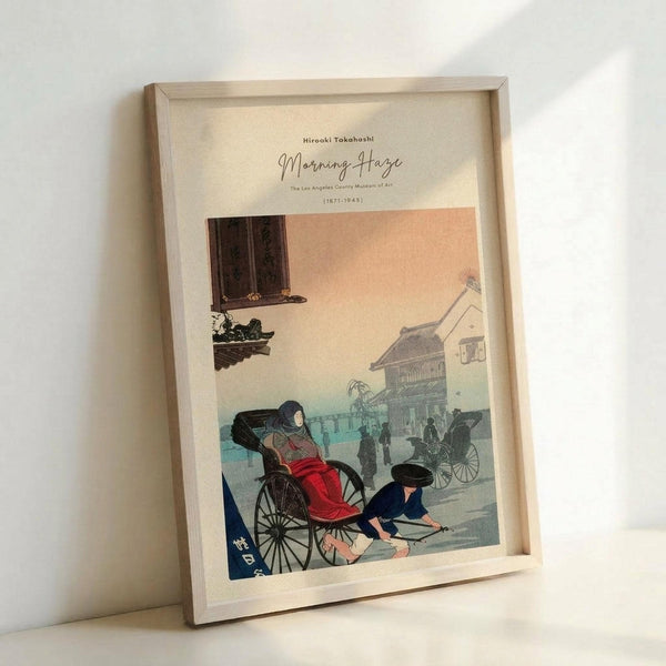 May include: Light wooden frame displaying a vintage Japanese woodblock print showing people with rickshaws on a misty street scene in soft peach, teal and coral tones. Frame leans against white wall on light surface, showing museum-style text at top with artist name and dates.