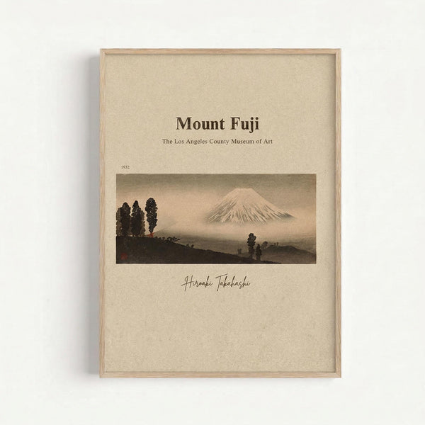 May include: Framed poster print displaying a vintage Japanese landscape artwork featuring Mount Fuji in muted earth tones. The mountain appears snow-capped against a hazy sky, with dark silhouetted trees and rolling hills in the foreground. Text above reads "Mount Fuji" and "The Los Angeles County Museum of Art" with "1952" and an artist signature below. Light wood frame on beige textured background with subtle shadows.