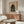 May include: A framed vintage-style poster featuring a dark silhouetted Japanese pagoda castle against a warm beige background with bare tree branches. The artwork hangs above a mid-century modern walnut credenza with sliding doors in a minimalist living room setting. A white curved lounge chair sits beside an oval glass coffee table with wooden base, while a sleek table lamp and floor lamp provide ambient lighting on neutral walls.