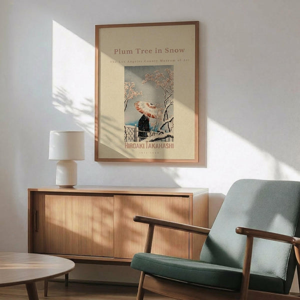 May include: Japanese woodblock print poster featuring a figure with red umbrella under snow-covered plum tree branches, displayed in wooden frame on white wall above mid-century modern wooden sideboard with ceramic table lamp, next to sage green upholstered armchair with wood arms in sunlit room