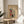 May include: Framed vintage Japanese woodblock print poster featuring a red torii gate, snow-covered buildings, and figures in winter scene. Warm beige matting in thin wooden frame, displayed on round wooden side table next to cream upholstered chair. Soft natural lighting creates shadows across neutral-toned room with plant visible in corner.