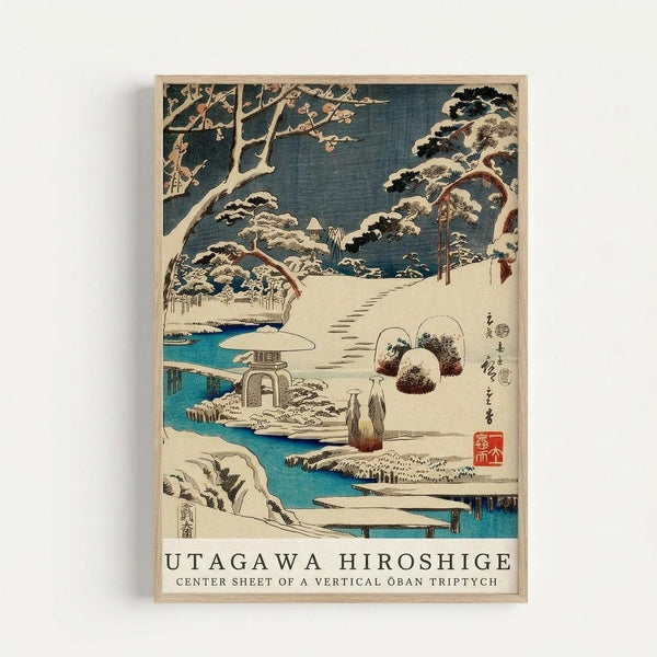 Japanese woodblock print featuring a snow-covered winter landscape with a stone lantern, curved bridge over turquoise water, and snow-laden pine trees. Two figures in traditional robes walk along a snowy path. The artwork displays classic ukiyo-e style with deep blue sky, white snow, and vibrant blue water. Text at bottom reads "UTAGAWA HIROSHIGE CENTER SHEET OF A VERTICAL OBAN TRIPTYCH". Print is displayed in a light wooden frame against white wall.