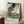 May include: Framed vintage Japanese woodblock print featuring a large black and white scaled carp kite against blue sky, with Mount Fuji and traditional village landscape below. The artwork displays red Japanese text columns and sits in a light wood frame on white carpet beside a coffee cup on wooden block and beige fabric chair in bright natural lighting.