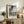 May include: Framed Japanese woodblock print featuring a large black carp kite with detailed scales floating above a landscape with Mount Fuji in the background. The artwork displays traditional ukiyo-e style with blue sky gradients and includes Japanese text. Print sits on rustic wooden sideboard next to fern plant, ceramic vase, and stacked books in warmly lit living room setting with cream upholstered chair visible.