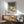 May include: Framed Japanese woodblock print showing winter landscape with snow-covered trees, traditional buildings, and blue water, displayed above wooden sideboard with table lamp in modern living room setting with sage green upholstered chair and round coffee table