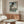 May include: Japanese woodblock print poster featuring large black koi fish with detailed scales swimming above landscape with bridge and Mount Fuji, displayed in thin wooden frame above mid-century modern walnut credenza in minimalist living room with white curved chair, glass oval coffee table, and wooden floor lamp