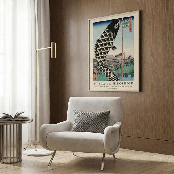 May include: Japanese woodblock print artwork featuring a large black koi fish with scaled pattern swimming above a landscape with bridge and buildings. The vintage-style poster is displayed in a light wood frame on wood paneled wall above a cream upholstered armchair with geometric patterned pillow. Modern brass floor lamp and side table with open book complete the neutral-toned living room setting.