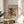 May include: Framed art print of Wassily Kandinsky's abstract painting featuring vibrant swirls of blue, yellow, red and green with geometric shapes and flowing lines. The beige matted poster sits on a light wood round side table next to a cream upholstered chair, with plant leaves visible in soft natural lighting against white walls.