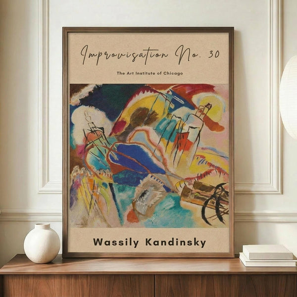 May include: A framed abstract art print displayed on a wooden sideboard against white paneled walls. The poster features vibrant swirling forms in blues, yellows, reds, and greens with dynamic brushstrokes and geometric elements. The print has cream matting and dark wood frame, with "The Art Institute of Chicago" and "Wassily Kandinsky" text. A small white ceramic vase and stacked books sit nearby on the warm wood surface.